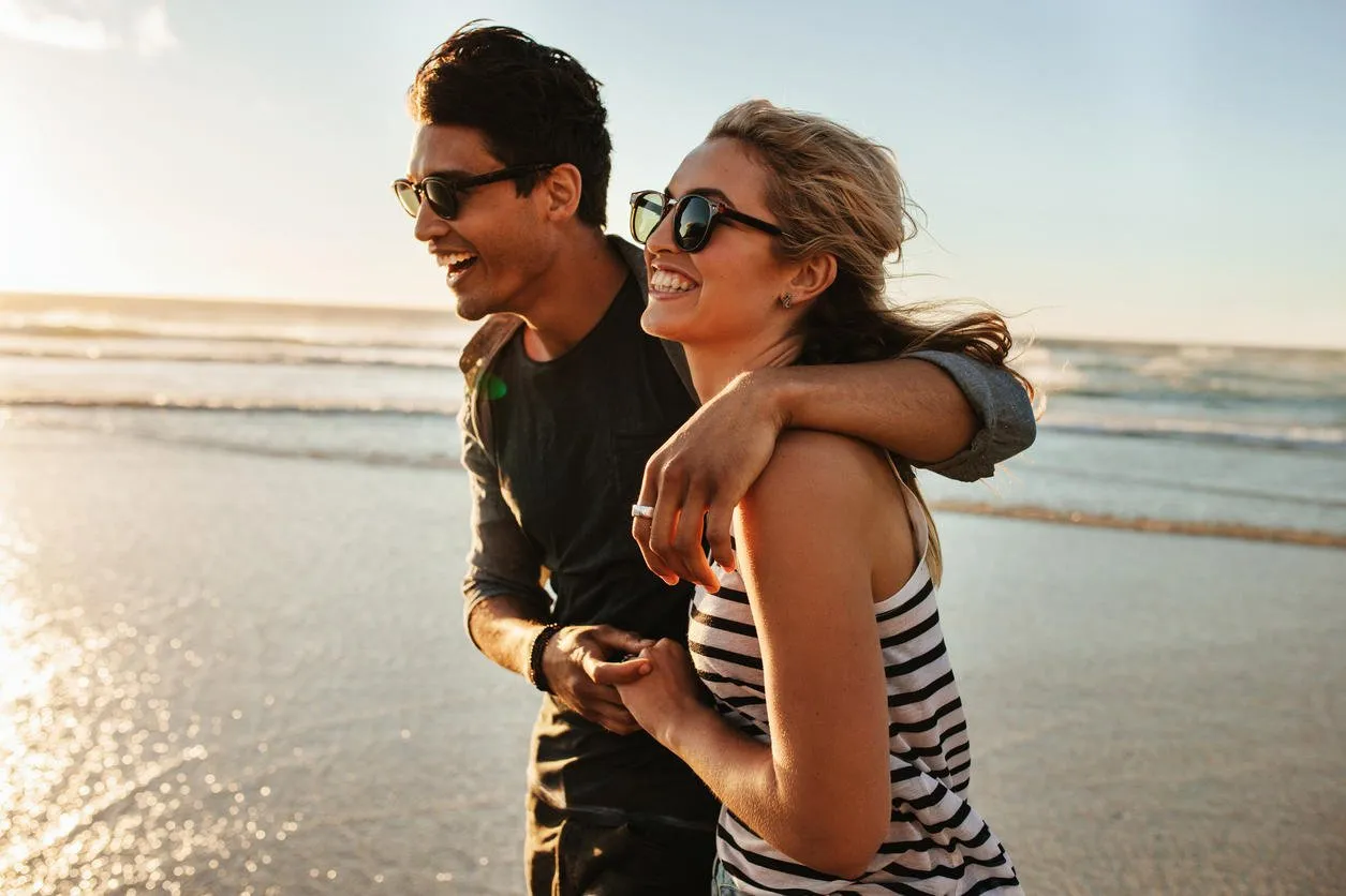outdoor shot of smiling young couple walking on beach young man and woman strolling together on seashore on a summer day