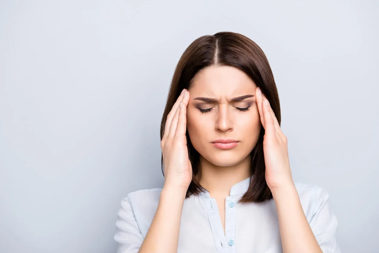 portrait of upset, sad, pretty, nice, charming, stylish woman in shirt having head ache, stress, troubles, touching temples with fingers and close eyes, standing over grey background