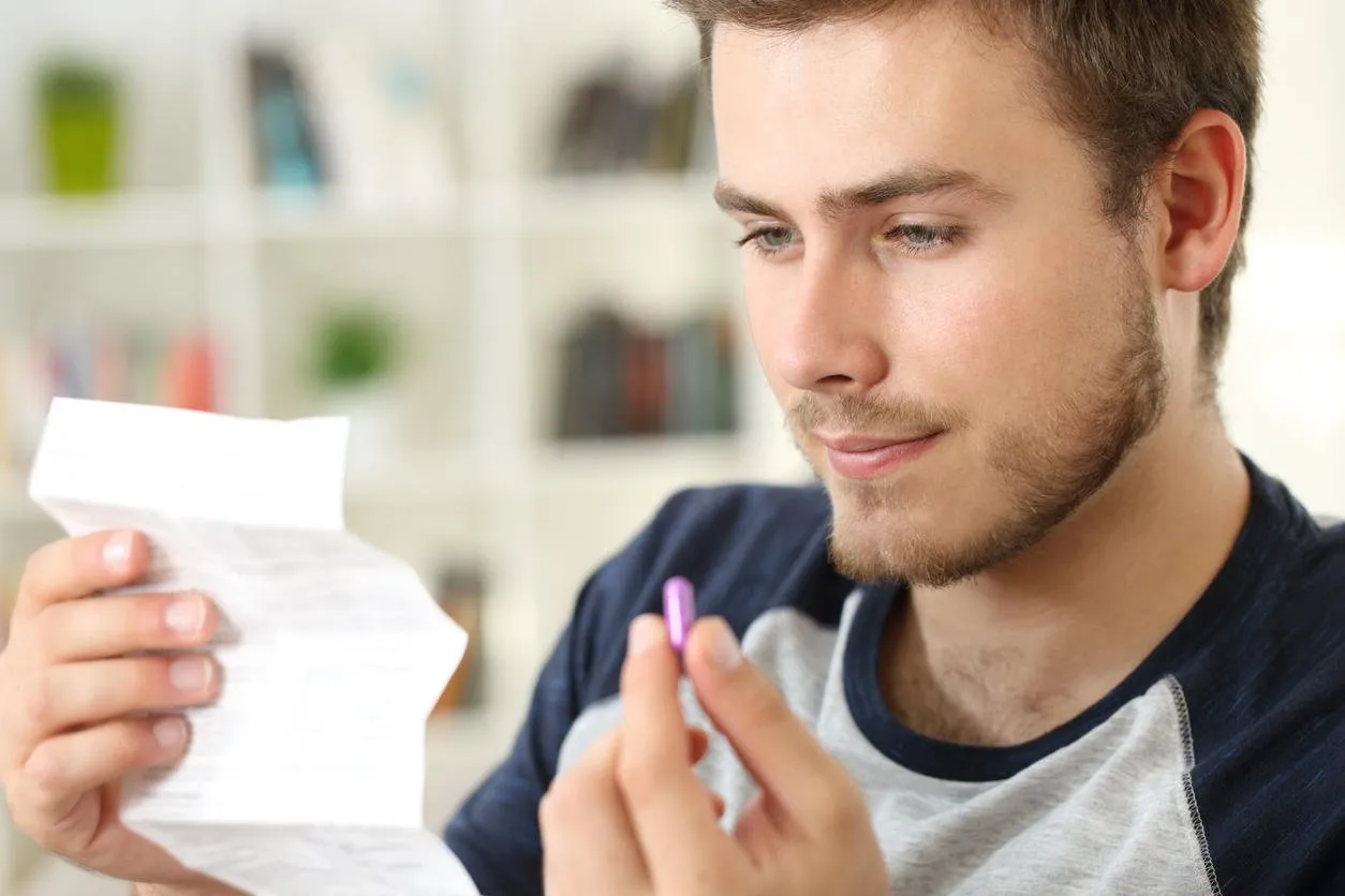 man reading a leaflet before to take a pink pill sitting on a sofa in the living room in a house interior