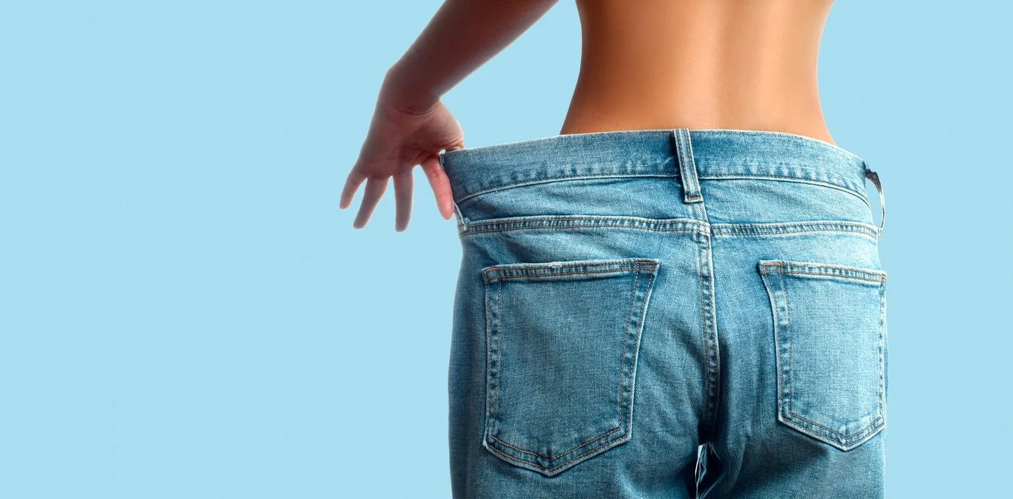 woman in oversize jeans after weight loss female bottom in oversize jeans on pastel blue background