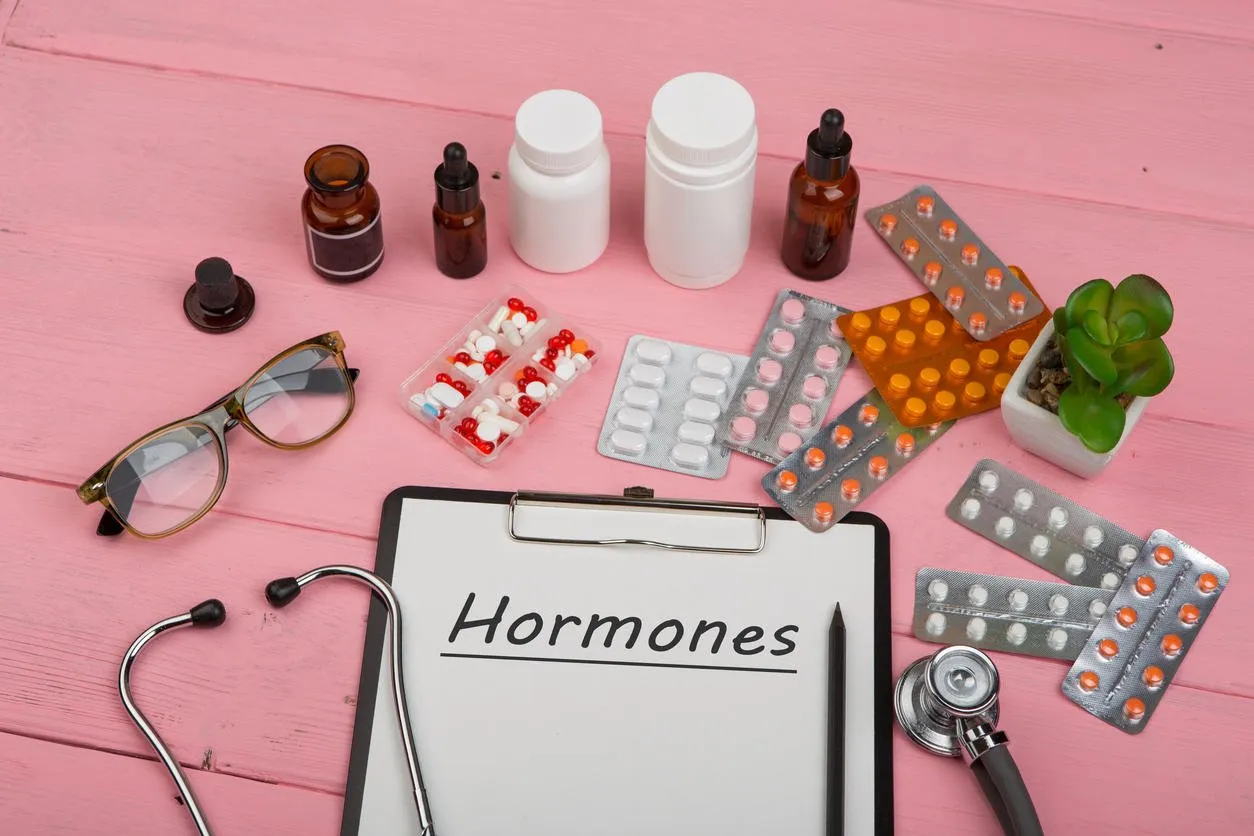 doctor workplace with clipboard and text hormones, medicine bottles, red stethoscope, eyeglasses and pills on pink wooden table medication prescription health care or illness