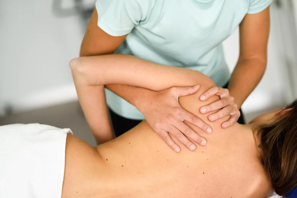 professional female physiotherapist giving shoulder massage to brunette woman in hospital medical check at the shoulder in a physiotherapy center