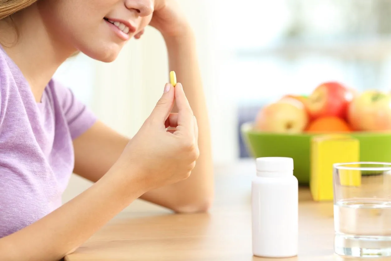 close up of a girl hand taking vitamin pill on a table at home with a window in the background and a colorful decoration