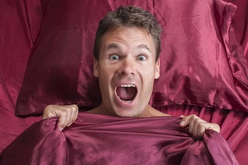 gros plan d'un homme caucasien terrifié réagissant au cauchemar et criant sous les draps rouges