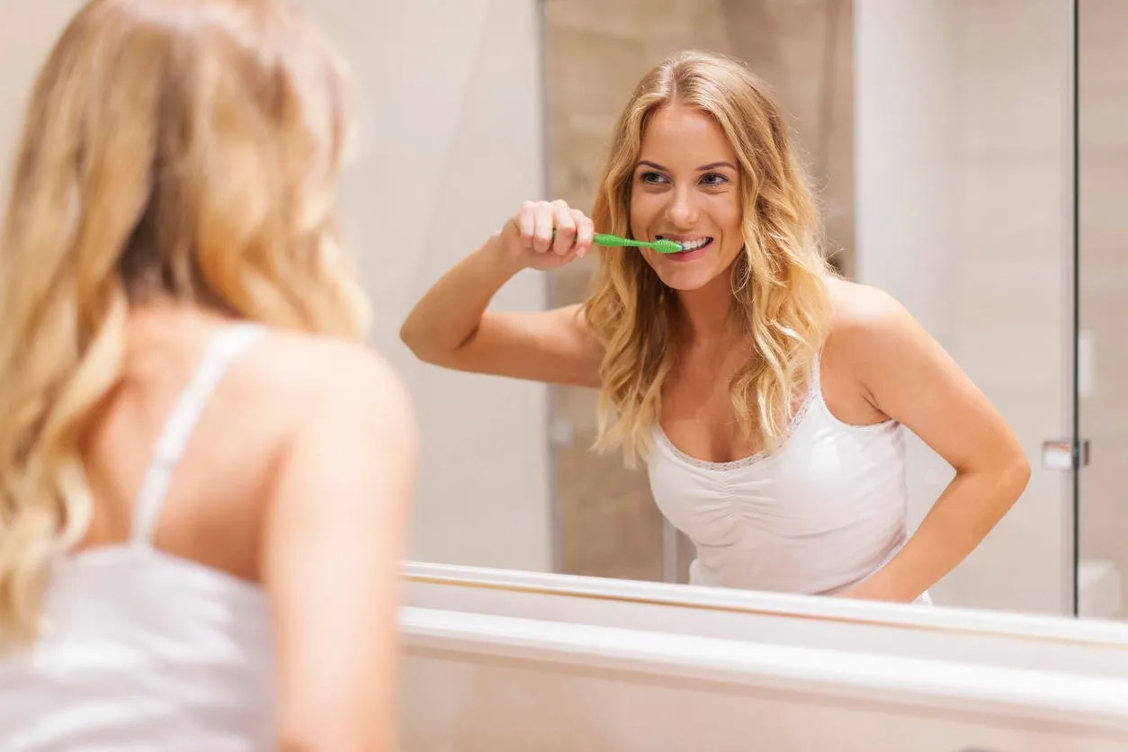 femme se brosser les dents devant le miroir
