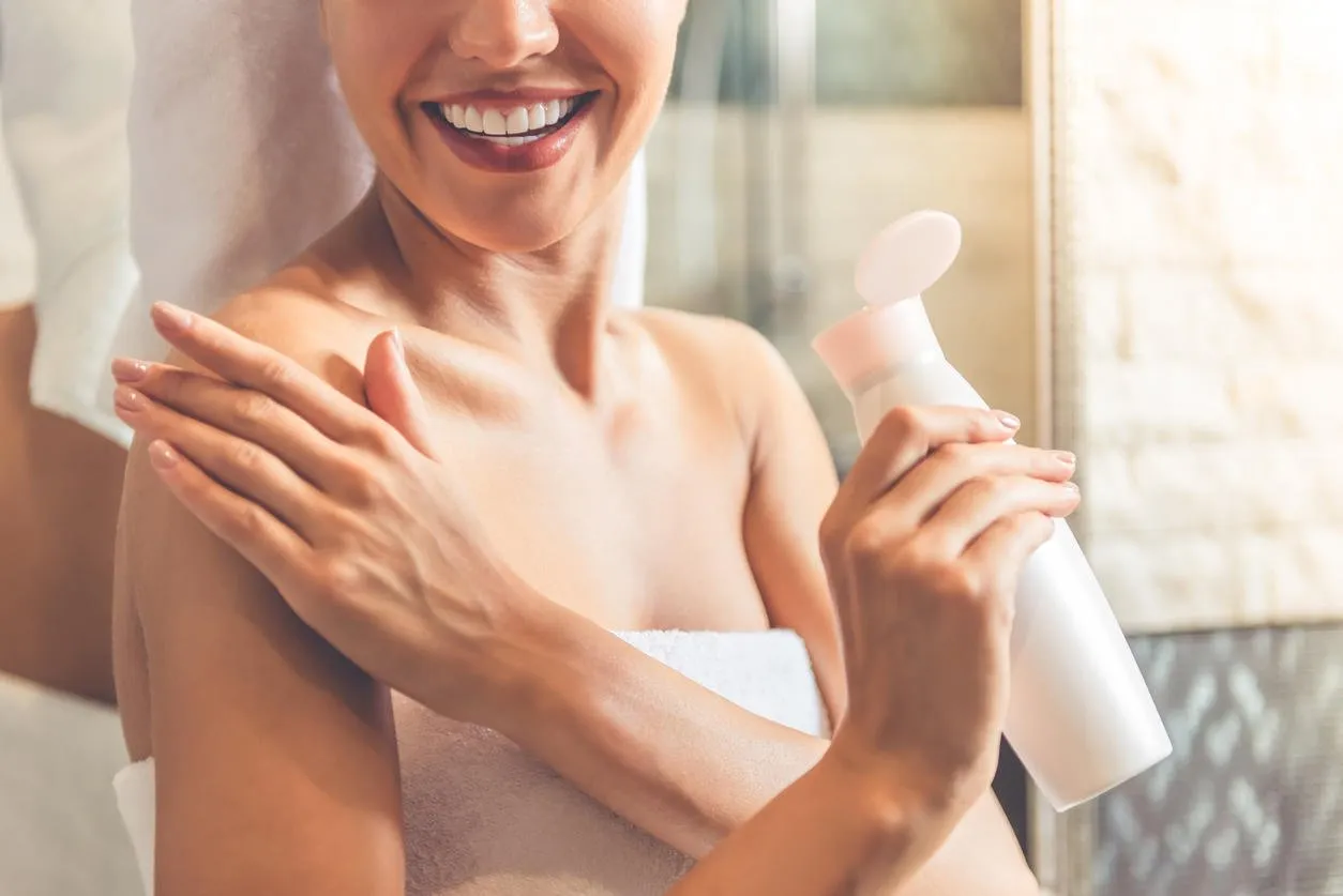 image recadrée de la belle jeune femme en serviette de bain appliquant la lotion pour le corps sur ses épaules et souriant tout en se tenant dans la salle de bain