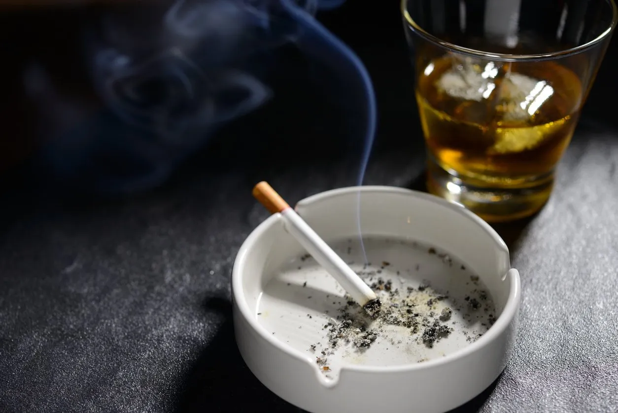 lit and smoking cigarette in ashtray with glass of whiskey