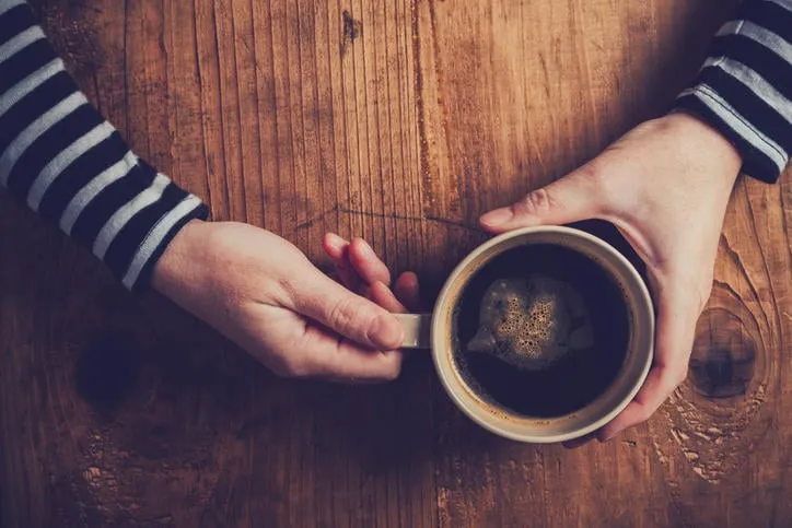 femme solitaire, boire du café le matin, vue de dessus des mains féminines tenant la tasse de boisson chaude sur le bureau en bois, rétro tonique