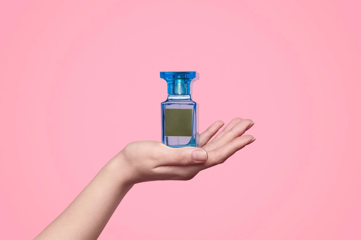 hand of anonymous model showing bottle of perfume with blank label against pink background