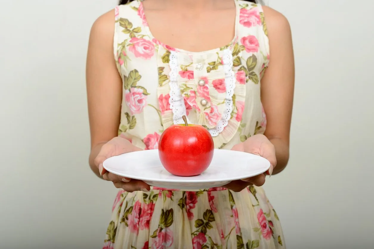 studio shot of beautiful woman indoors holding red apple on white plate