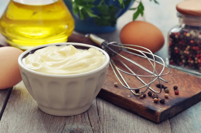 homemade mayonnaise in bowl with oil, eggs and spice on wooden background