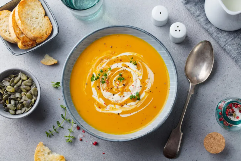 pumpkin and carrot soup with cream on grey stone background top view