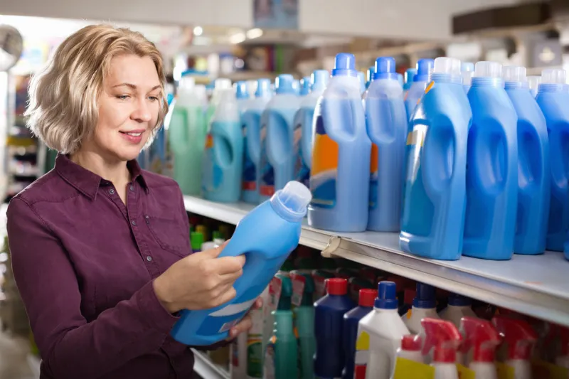 positive glad female with selecting fabric conditioner in household store