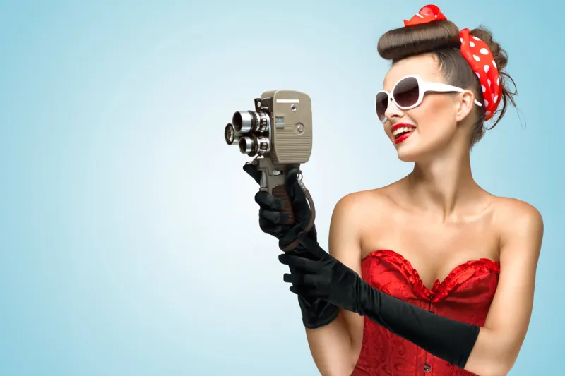 a photo of the pin-up girl in corset and gloves holding vintage 8mm camera