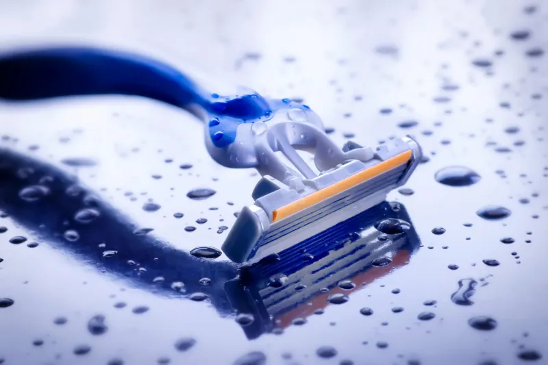 wet disposable razor on blue background with water drops
