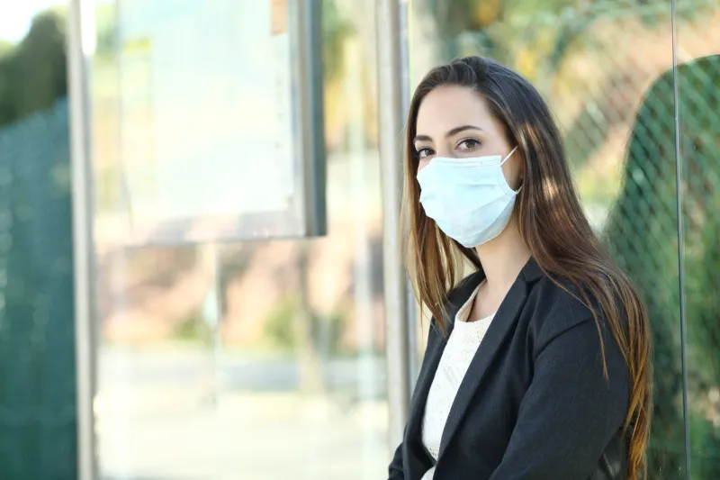 woman wearing a mask to prevent contagion sitting in a bus stop waiting for transport