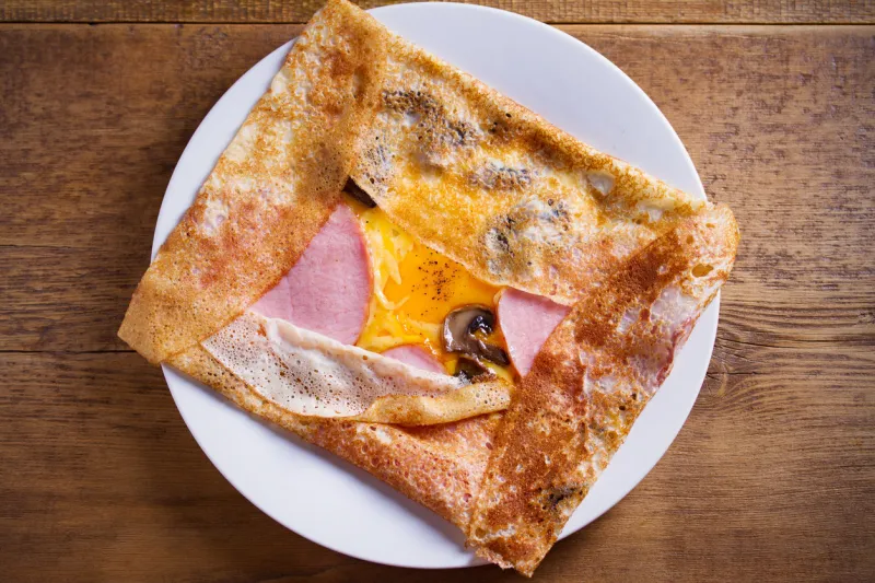 crepes, thin pancakes with ham, cheese, egg, and mushrooms pancakes with filling on white plate