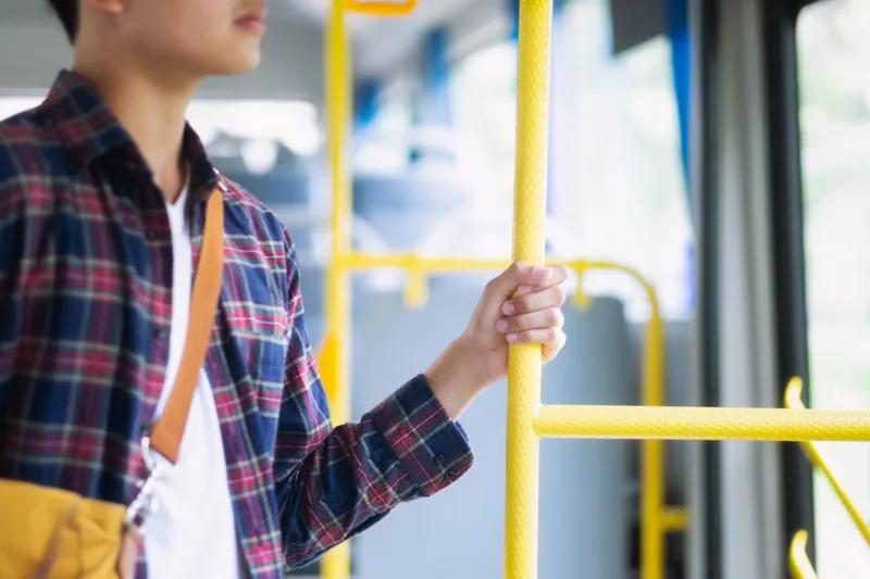 young asian man holding handle on the public bus