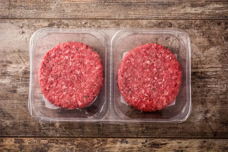 burger meat packaged in plastic on wooden table