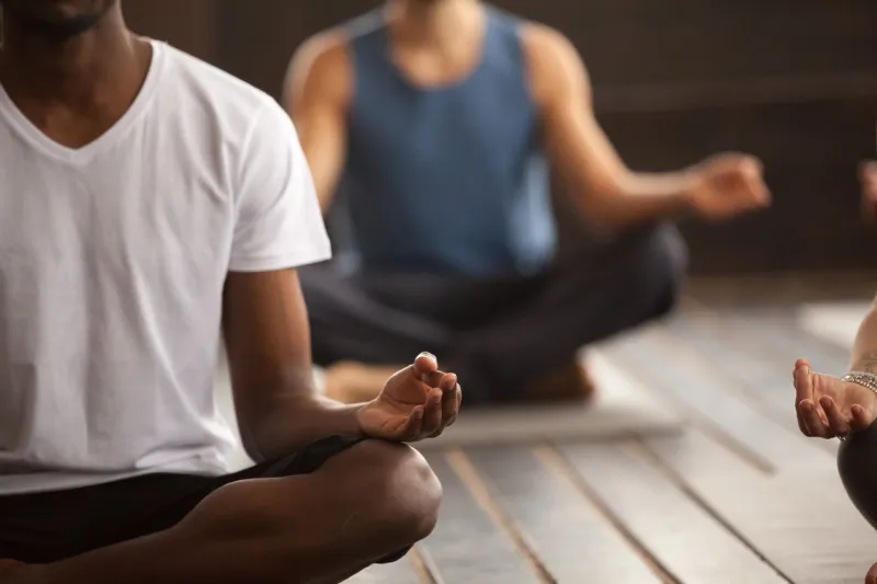 young black man and a group of young sporty people practicing yoga lesson, sitting in sukhasana exercise, easy seat pose, working out, indoor close up focus on mudra gesture, studio room