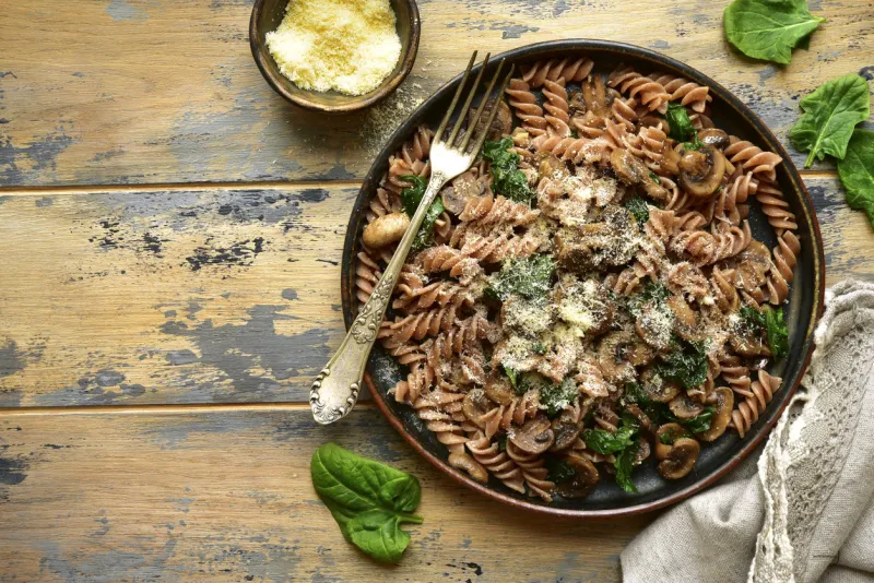 whole wheat fusilli pasta with mushroom and spinach on a dark plate over old rustic wooden backgroundtop view with copy space
