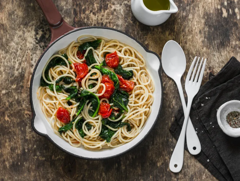 vegetarian whole grain spaghetti pasta with cherry tomatoes and spinach sauce in a cast iron pan on a wooden background, top view copy space, healthy diet food concept