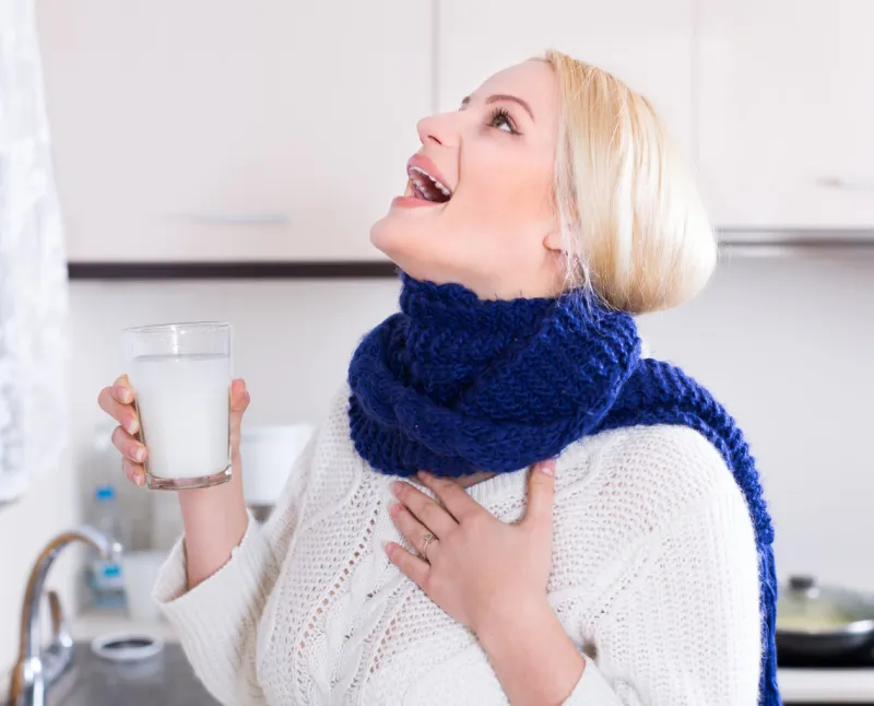 blonde young woman having pain in throat and doing oral rinsing at kitchen
