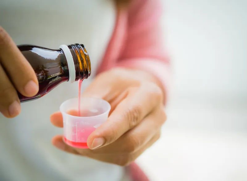 closeup woman pouring medication or antipyretic syrup from bottle to cup healthcare, people and medicine concept