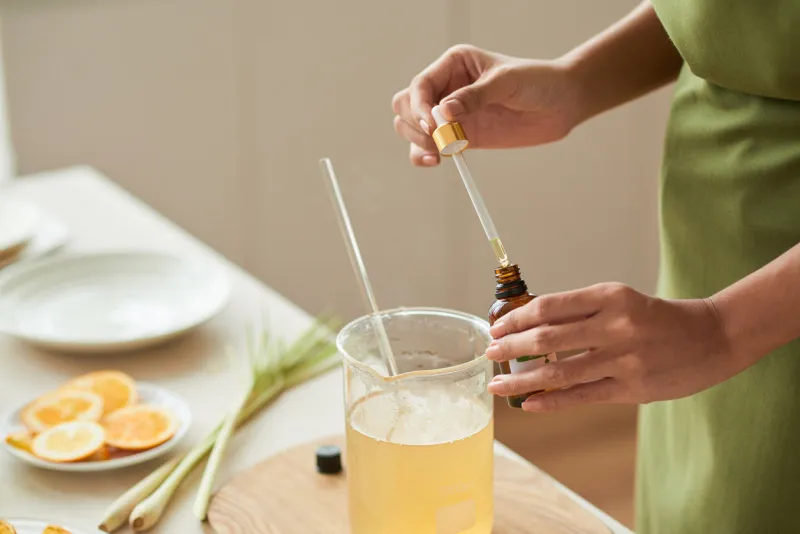 hands of woman adding essential oil into melted soap base