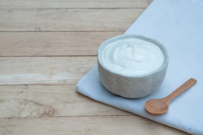 natural homemade plain organic yogurt in ceramic bowl and wood spoon on wood texture background, copy space