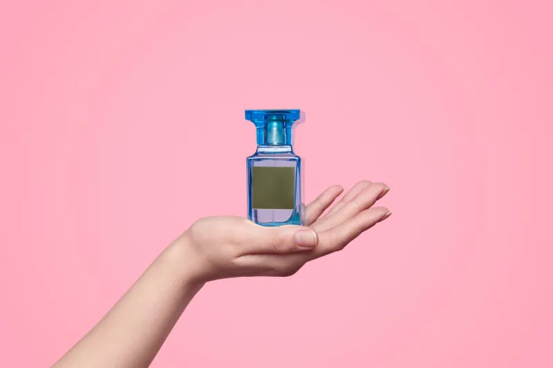 hand of anonymous model showing bottle of perfume with blank label against pink background