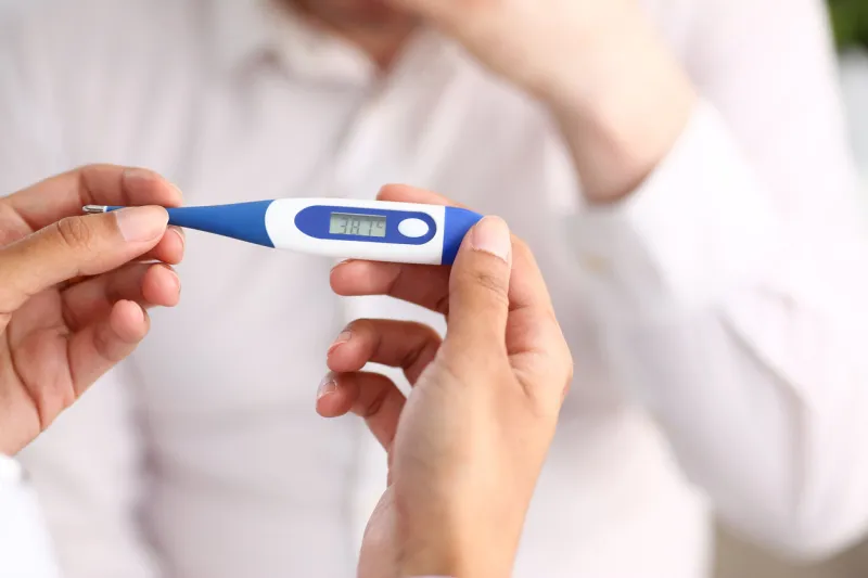 hands of a female doctor holding a thermometer with a patient's high temperature in hand