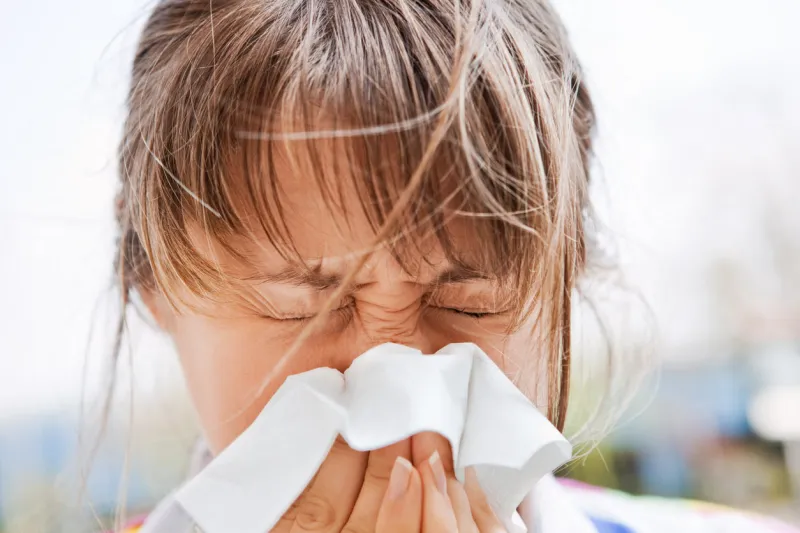 a young woman blowing her nose outdoors