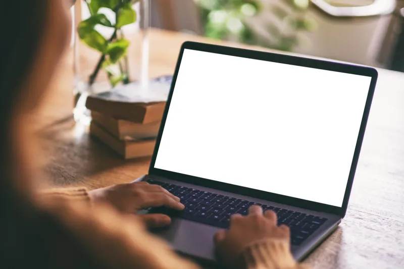 mockup image of a woman using and typing on laptop with blank white desktop screen on wooden table