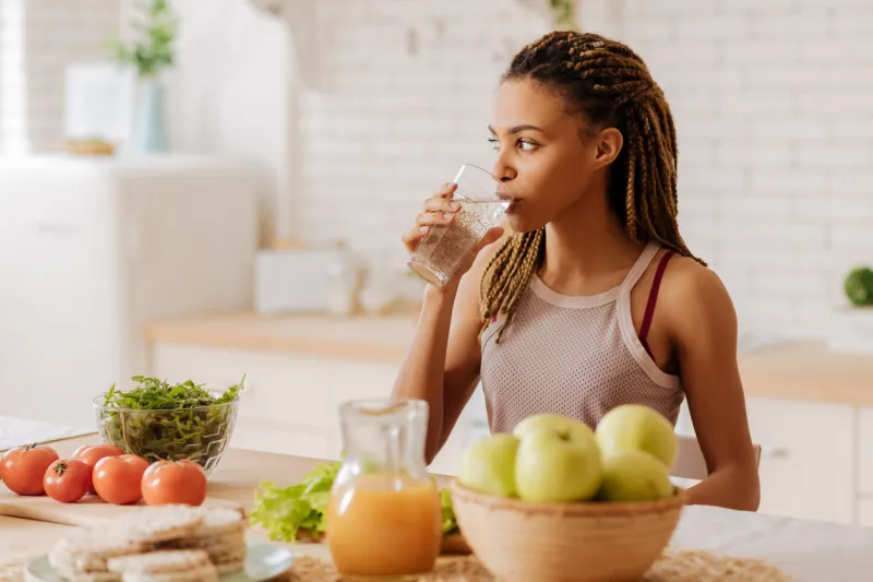 water before breakfast slim and fit woman with many little braids drinking water before having breakfast