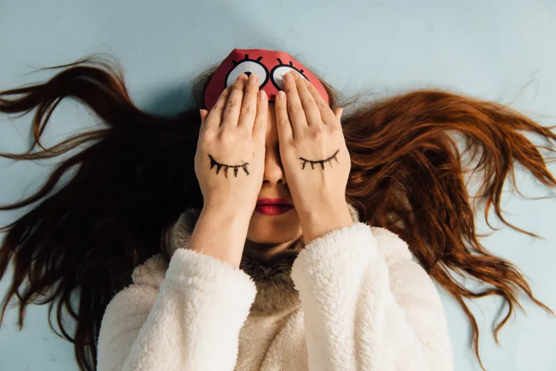 young beautiful girl in a sweater with a deer and a sleep mask lying down on white background