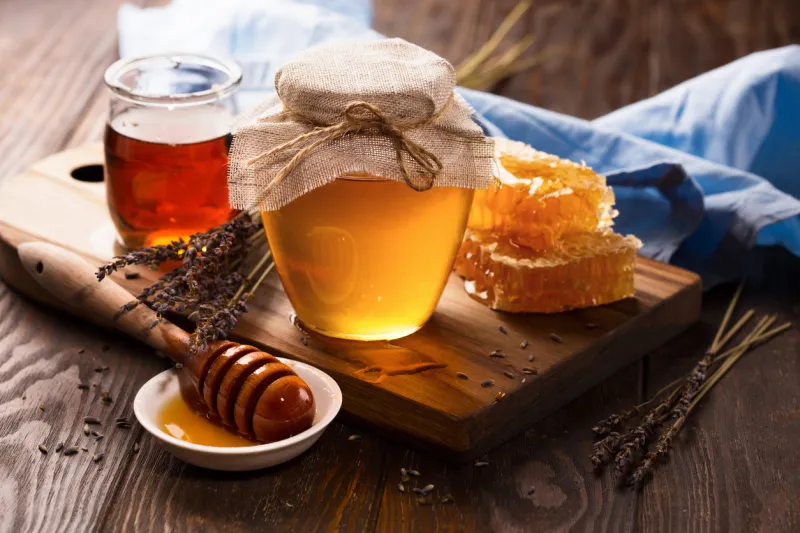 jar of liquid honey with honeycomb inside and bunch of dry lavender over old wooden table dark rustic style, selective focus