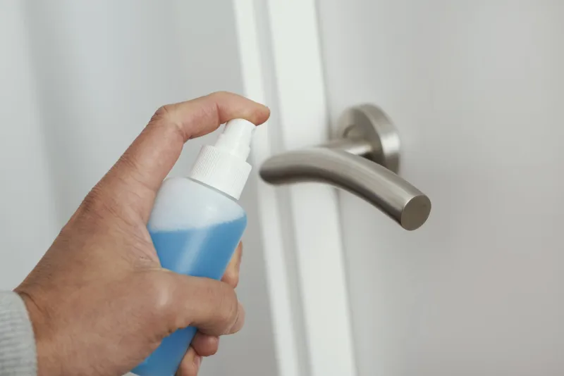 closeup of a caucasian man disinfecting the door handle by spraying a blue sanitizer from a bottle