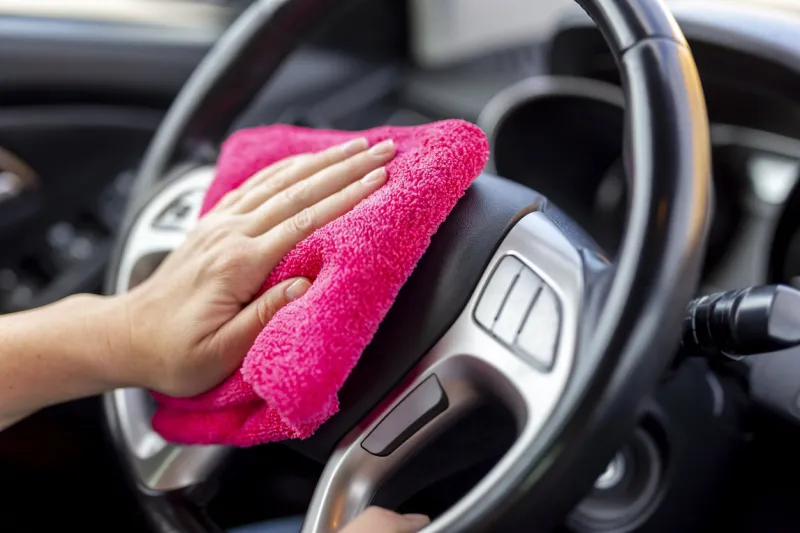 detail of female hand wiping dust and polishing car interior parts with cleaning cloth