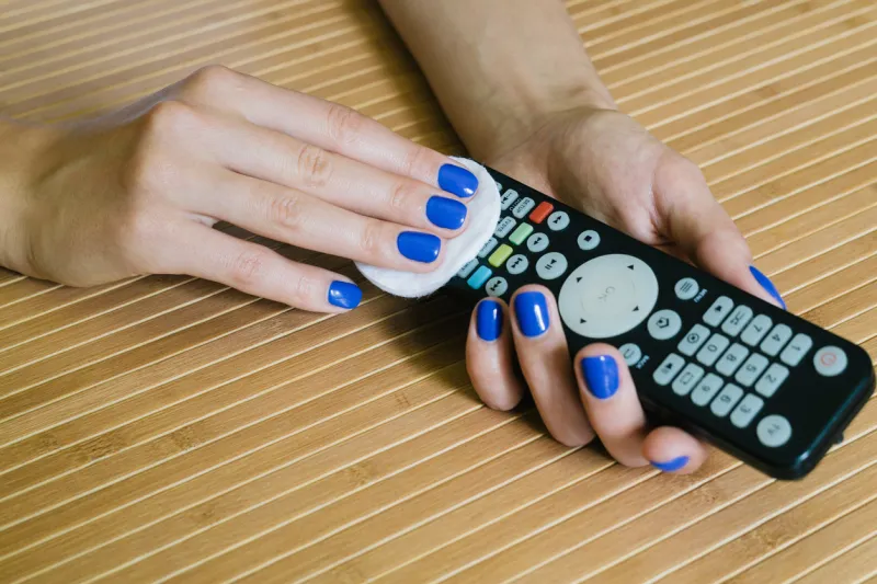 female hands with blue manicure wipe the remote control at the wooden table