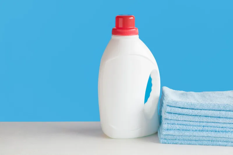 white plastic, liquid detergent bottle and light blue towels fabric softener for clothes washing laundry care chores of housewife regular washing empty place for text or logo front view