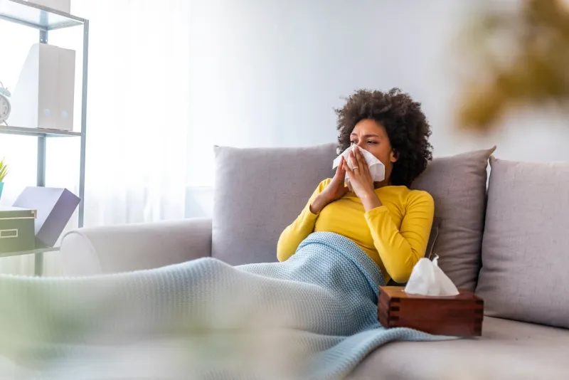 the sick woman, holding a handkerchief, sneezing and feeling freezing, lying on the bed, at home health problem sick african american woman lying on the sofa