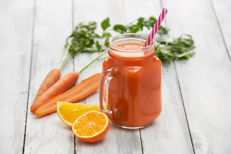 juice in a glass container surrounded by fresh vegetables and fruits on white boards