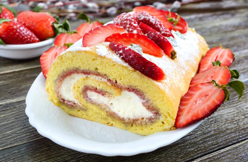 sweet biscuit roll with strawberries and cream on a wooden background