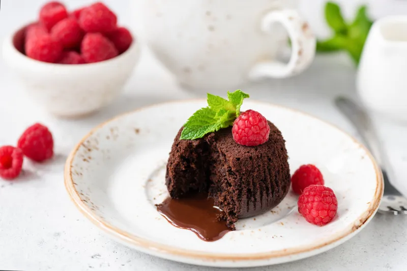 chocolate lava cake with molten core on white plate served with fresh raspberries and mint leaf