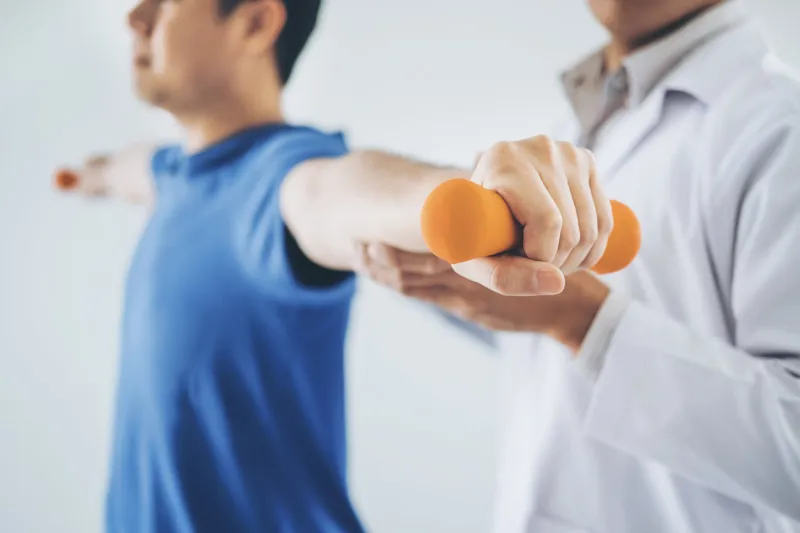 physiotherapist man giving exercise with dumbbell treatment about arm and shoulder of athlete male patient physical therapy concept