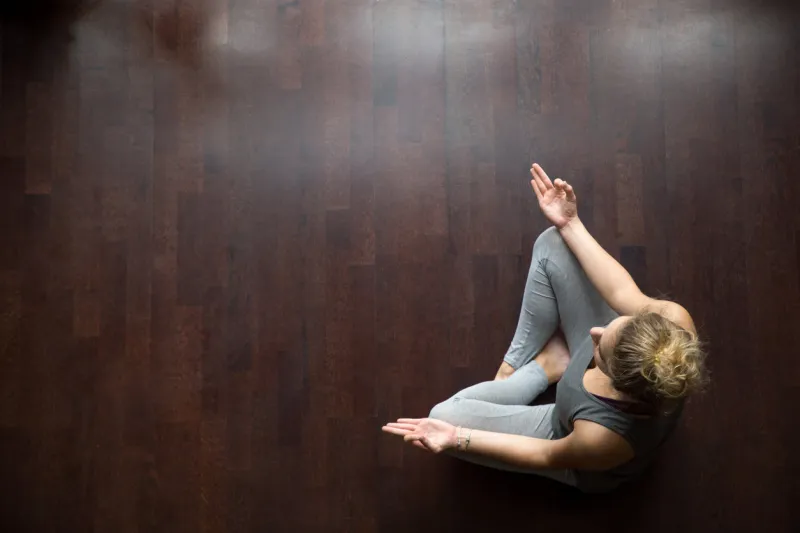 attractive young woman working out indoors, doing yoga exercise on wooden floor, sitting in easy (decent, pleasant posture), meditating, breathing, relaxing full length top view copy space