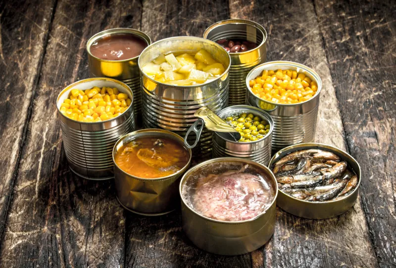 various canned vegetables, meat, fish and fruits in tin cans on a wooden background