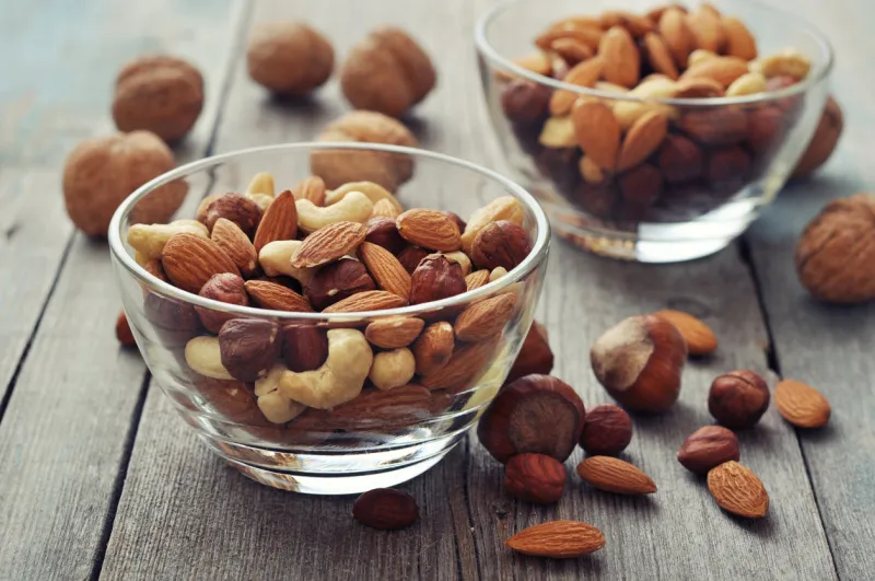 almonds, walnuts, cashew and hazelnuts in glass bowls on wooden background