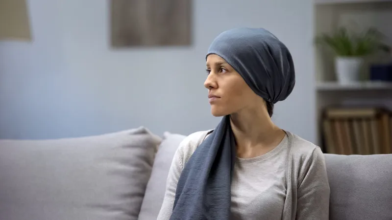 upset young lady in headscarf lonely sitting on sofa in oncologic hospital